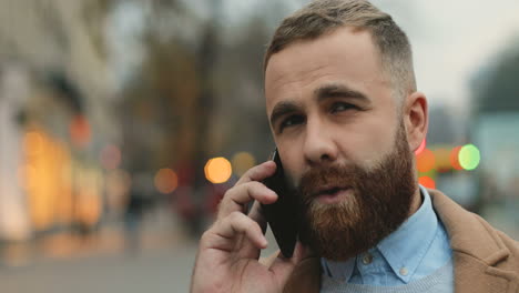 close-up view of caucasian businessman with a beard talking on the phone in the street in autumn