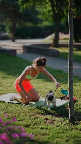 woman practicing yoga with her pug in the park