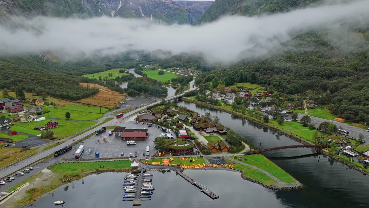 Vista aérea del pueblo de Gudvangen enmarcado por imponentes paredes de montañas nubladas, Noruega.