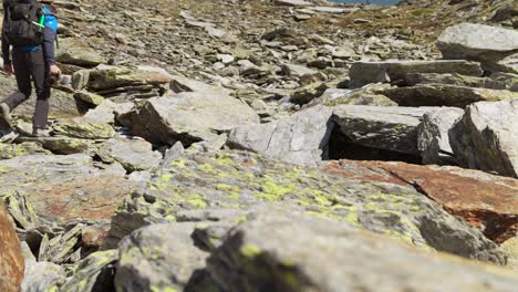 Male-Hiking-Content-Creator-Holding-Camera-Walking-Up-Rocky-Mountain-Hillside