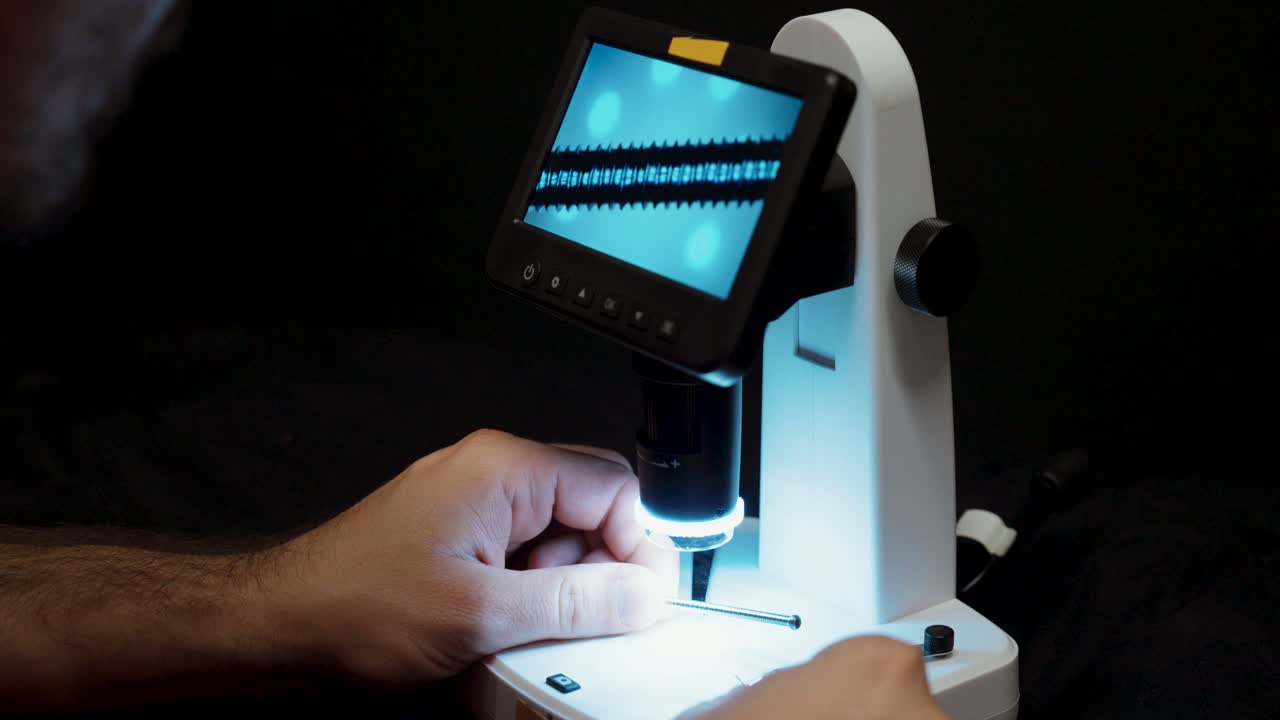 Close-up view of hands operating a digital microscope, adjusting focus and examining samples with precision and laboratory accuracy