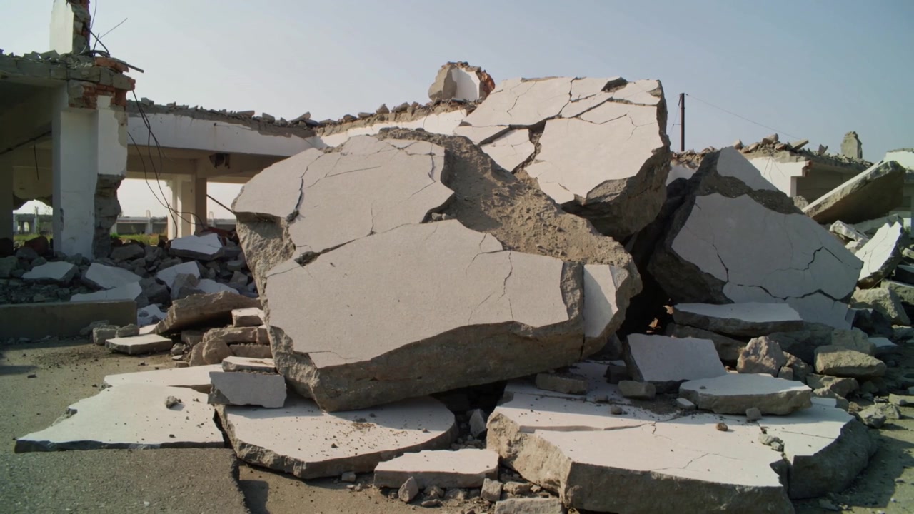 Showing collapse leaving centered pile of concrete slabs occupying demolition site, exposing rebar