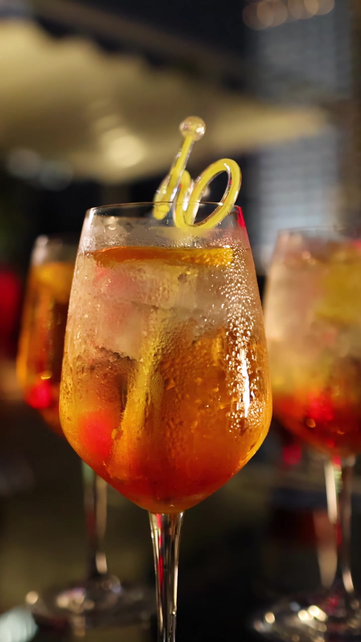 A group of young adults enjoy cocktails at a stylish nighttime party, with the camera shifting focus from drinks to lively conversation and laughter
