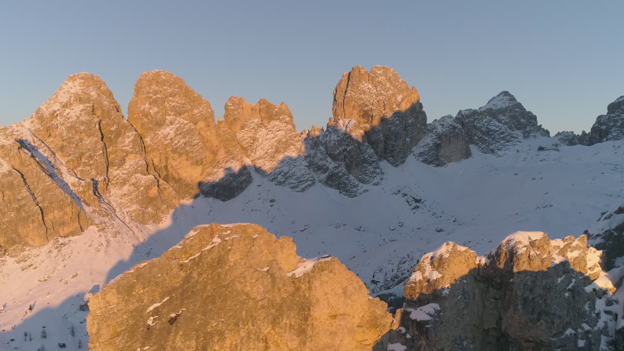Cime montuose aspre, innevate e luminose delle Tre Cime, vista aerea che rivela un'alba dorata su un crinale lontano.