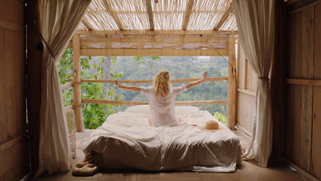 young woman lying in bed at tropical hotel resort enjoying vacation relaxing in comfort with view of jungle