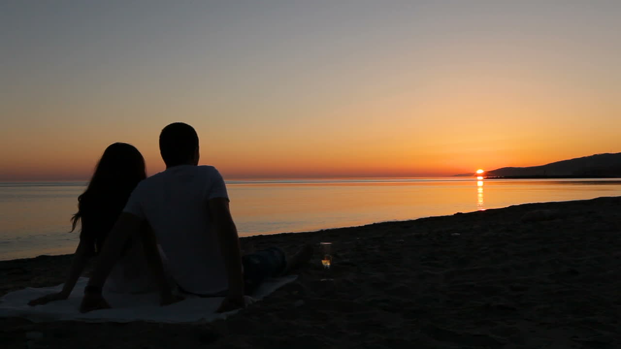 Couple sitting on beach. Back view of young couple sitting and enjoying sunset on beach