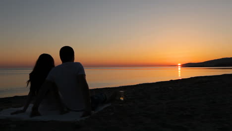couple sitting on beach. back view of young couple sitting and enjoying sunset on beach