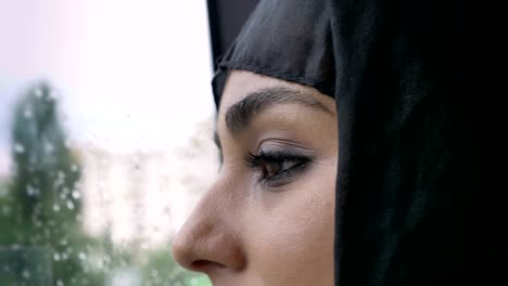 young muslim woman's in hijab eyes is watching in rainy window in bus, weather concept, transport concept, urban concept, dreaming concept, side view