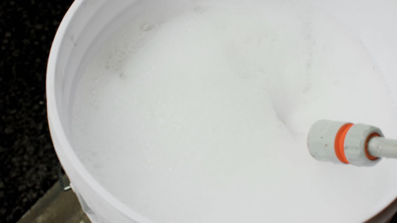 Filling a bucket with soapy water from a garden hose. Foam rising to the top. Static 4k shot.