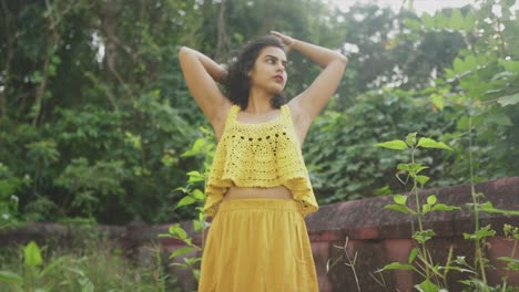 Young-Indian-woman-with-yellow-Crochet-outfit-makes-her-hair-in-the-outdoor,-garden