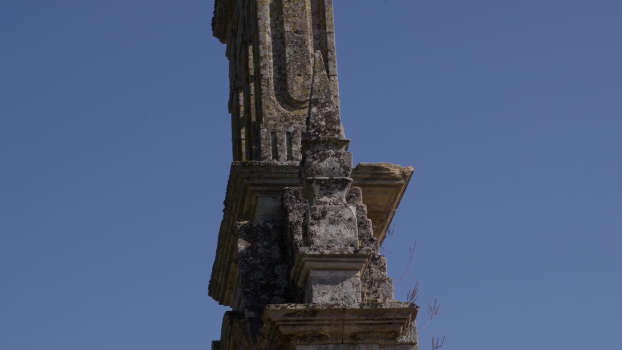 Close-up detalhado de um monumento de pedra antigo e desgastado com entalhes intrincados, capturado sob luz do dia brilhante e céu azul claro.