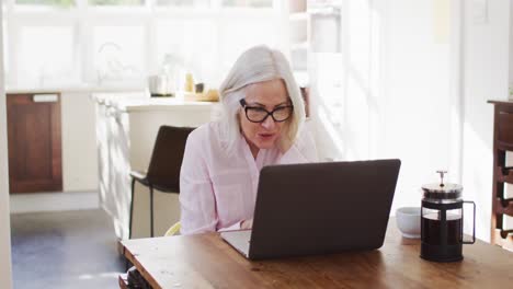 senior woman wearing glasses waving while having a video chat on her laptop while working from home