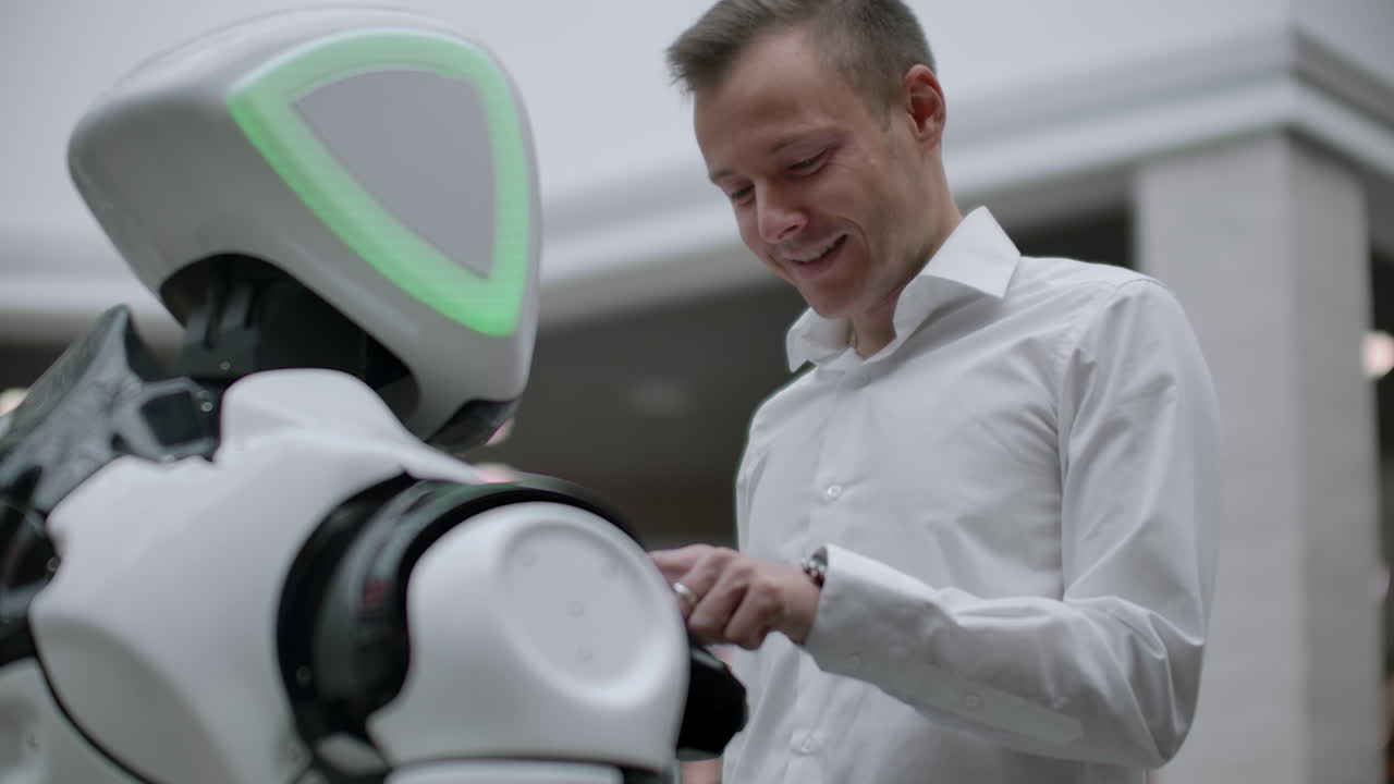 A man in a shirt communicates with a white robot asking questions and pressing the screen with his fingers