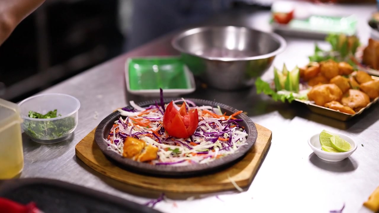 Close-up of chef hands arranging spicy chicken tikka on a garnished sizzling platter in Bangkok.