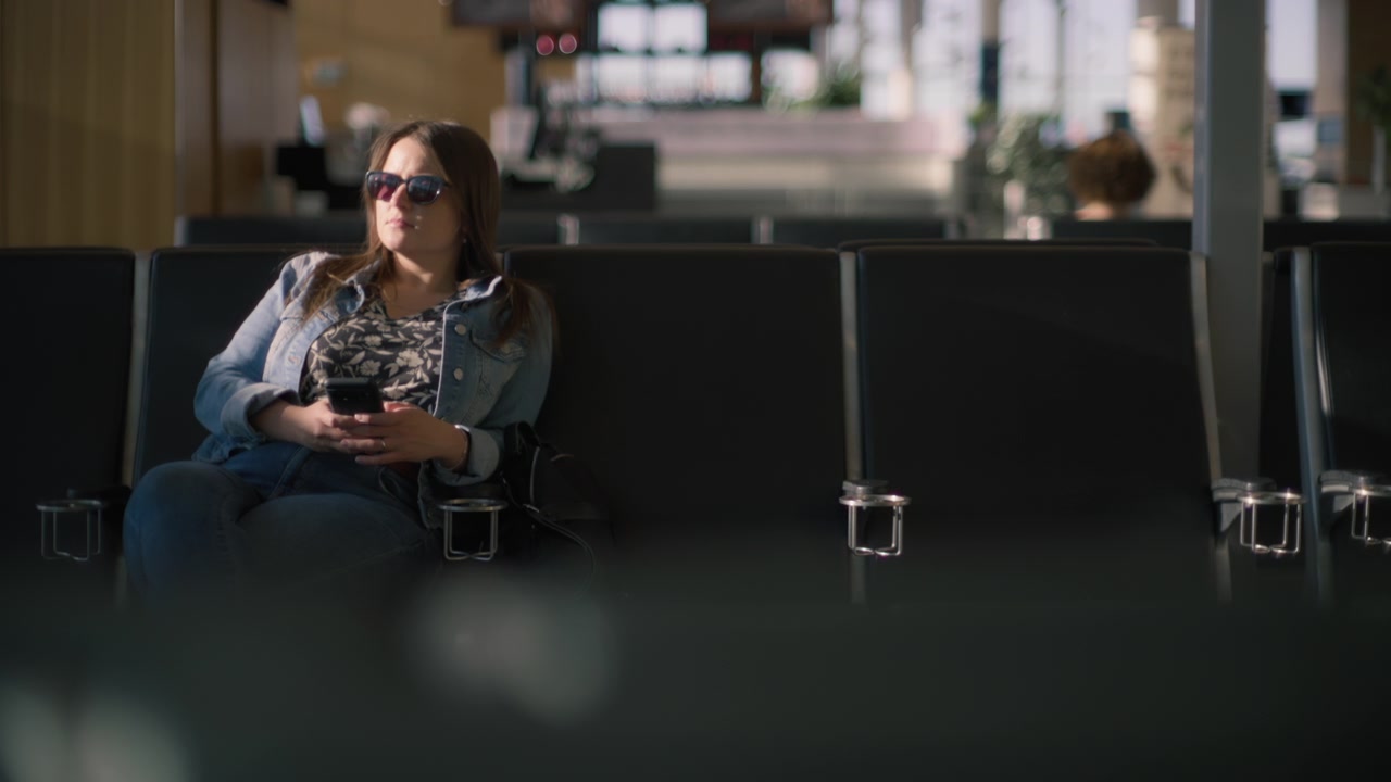 Una giovane donna seduta nella sala d'attesa del terminal dell'aeroporto con il suo telefono