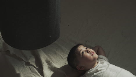 kid rests alone on floor near punching bag in gym. dreaming little asian boy lies thinking about victory in martial arts class slow motion. junior athlete