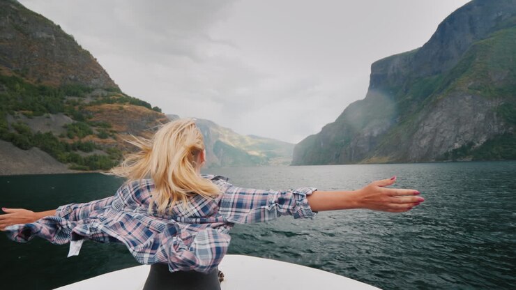 Eine freie Frau steht mit ausgebreiteten Armen am Bug eines Kreuzfahrtschiffes, das durch die Fjorde reist.