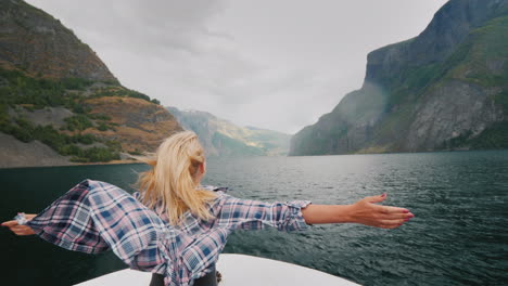 eine freie frau steht mit den händen an den seiten am bug eines kreuzfahrtschiffes, das die fjorde von bereist