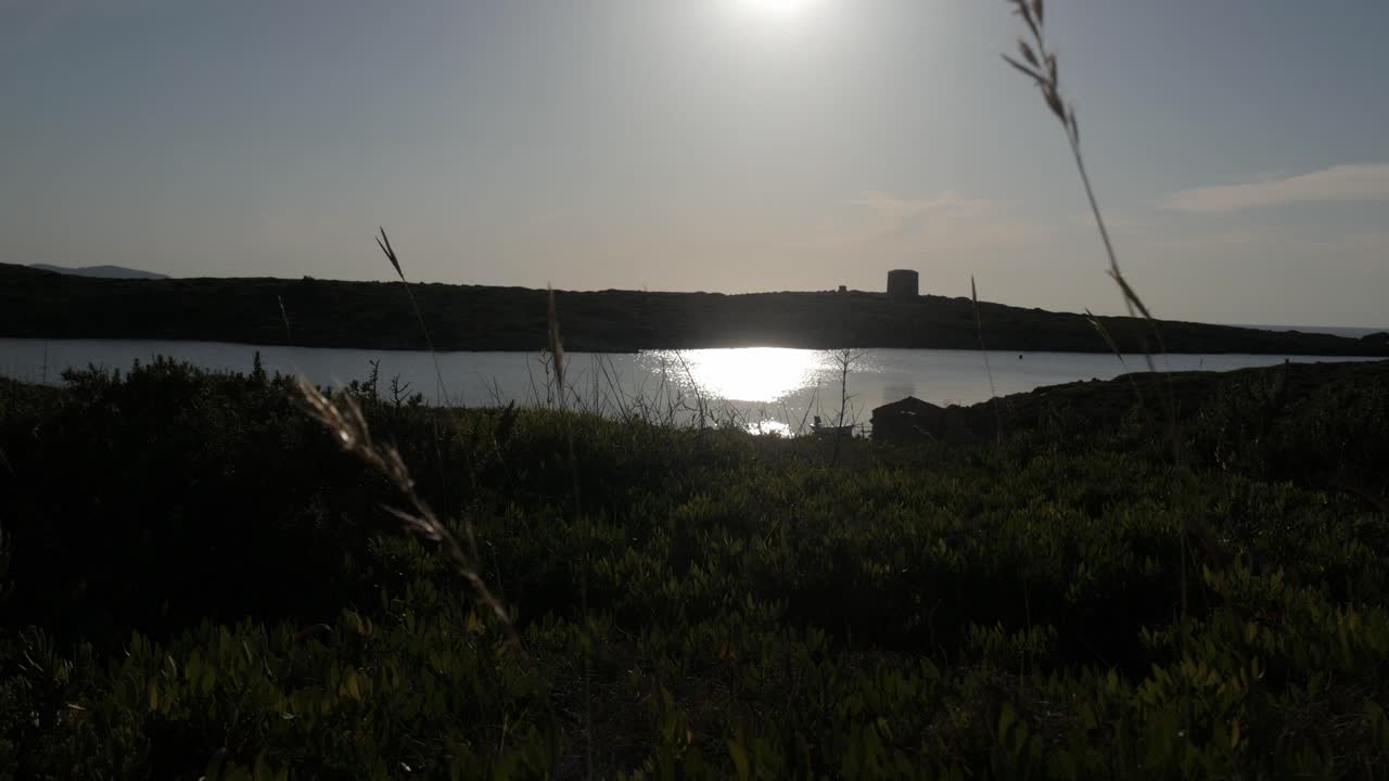 Sunlit coastal landscape with Torre De Sanitja, calm water, and natural scenery