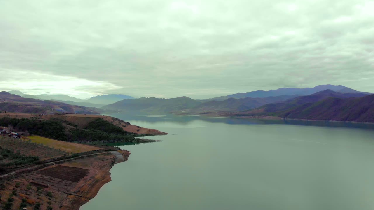 흐린 날에 새 나무와 보육원이 심어진 잔잔한 물 표면 세척 언덕 해안선이 있는 산 호수