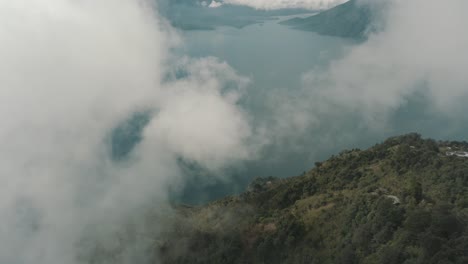 drone aerial flying high over the clouds, mountain cliff with trees revealing lake atitlan, guatemala