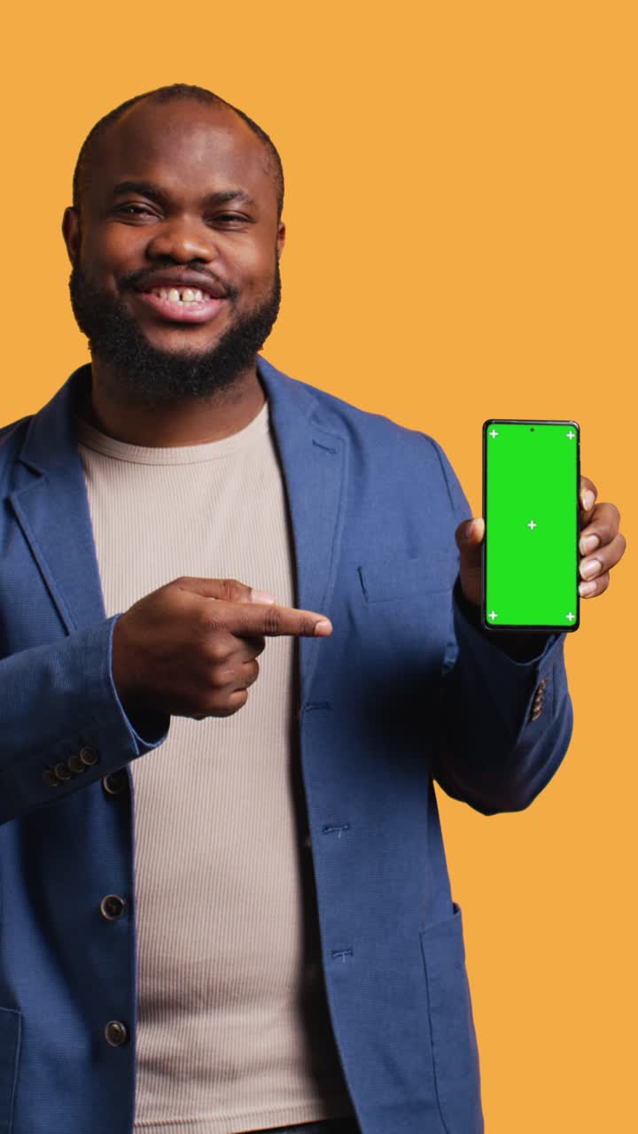 Vertical video Man presents phone with green screen display, isolated over studio background