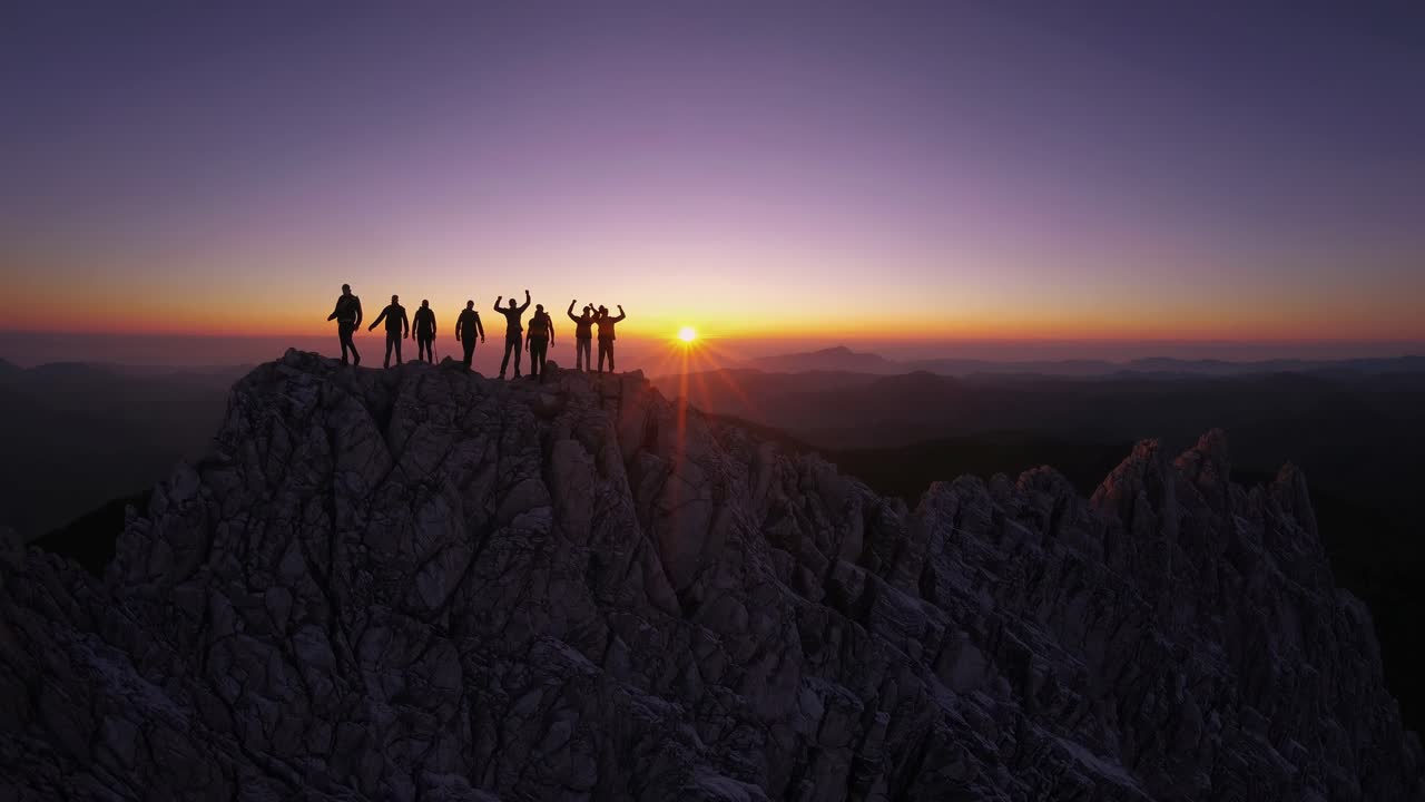 A breathtaking aerial video captures silhouettes on a mountain peak at sunset, showcasing a stunning
