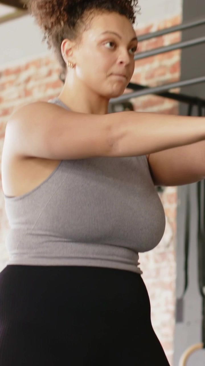 Video verticale: Donna adulta che espira, che oscilla un kettlebell da 5 kg per allenamento di forza in palestra, con top grigio.