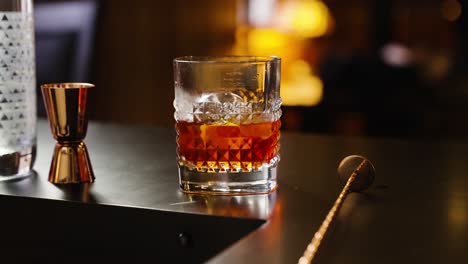 Negroni-Cocktail-Mit-Sphärischem-Eis,-Das-Auf-Einer-Bar-Mit-Jigger-Und-Rührstab-Beleuchtet-Wird