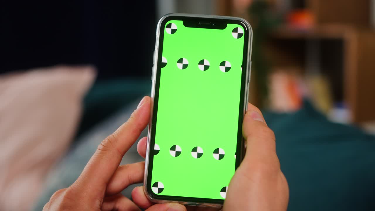 primer plano de una mano de hombre sosteniendo una maqueta verde pantalla clave de croma teléfono inteligente. teléfono móvil en el fondo atmósfera acogedora de loft casero