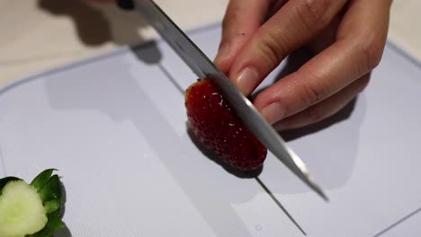 hands slicing a strawberry on a cutting board