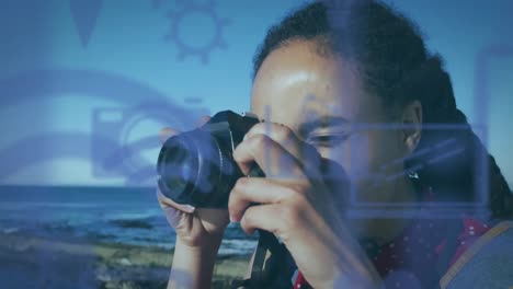 animation of technological icons over woman taking pictures by the sea