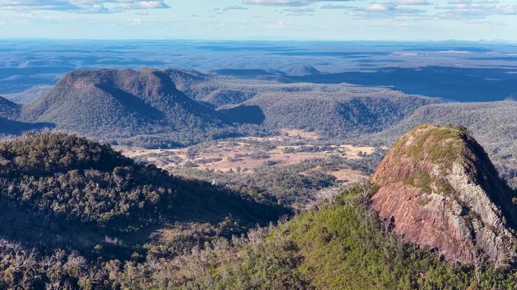 Un drone sorvola aspre formazioni rocciose e colline boscose nel Parco Nazionale Warrumbungle, Nuovo Galles del Sud, sotto una calda luce del tramonto