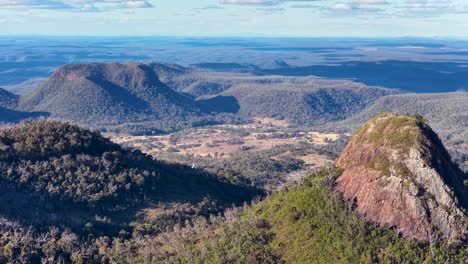 drone camera glides over rugged rock formations and forested hills in warrumbungle national park, new south wales, under warm sunset lighting