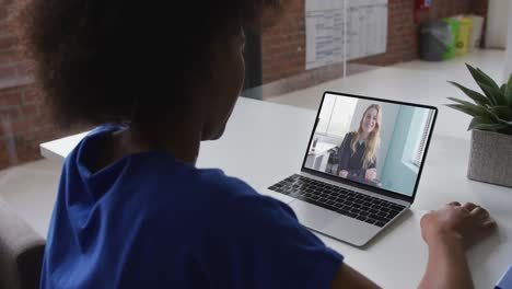 Rückansicht-Einer-Afroamerikanischen-Frau,-Die-Im-Büro-Einen-Videoanruf-Mit-Einer-Kollegin-Auf-Einem-Laptop-Führt