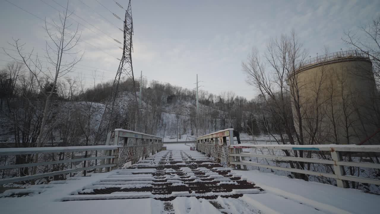 Belgo factory abandoned bridge in Shawinigan Quebec Canada with camera pushing forward over snow covered metal walkway, graffiti railings and winter industrial ruins