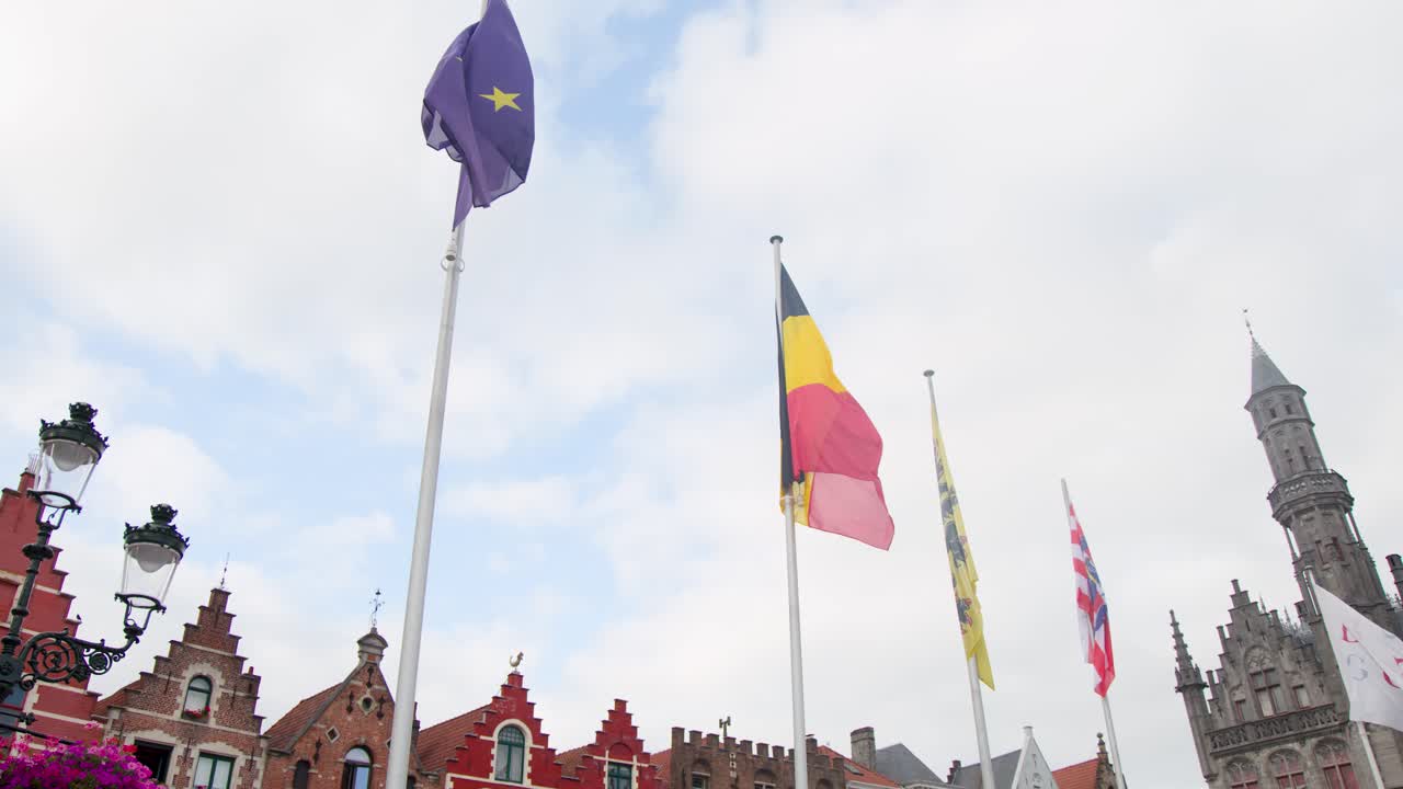 Bandiere che sventolano sopra l'architettura medievale nella storica piazza del mercato di Bruges, illuminate dalla luce del giorno