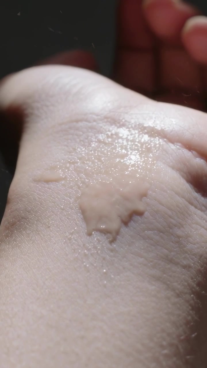 Vertikal video: Dyse påfører beige serum på håndled i studie, viser tekstureret glans.