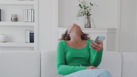 joven hermosa mujer afroamericana con teléfono en las manos se ríe se sienta en el sofá