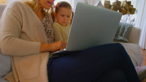 vista lateral de una joven madre caucásica enseñando a su hija usando una computadora portátil en un cómodo hogar 4k