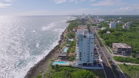 aerial orbiting shot of luxury hotel area with sea view on caribbean sea during sunny day in juan dolio, dominican republic - road along coastline and sunlight reflection on water surface - wide shot