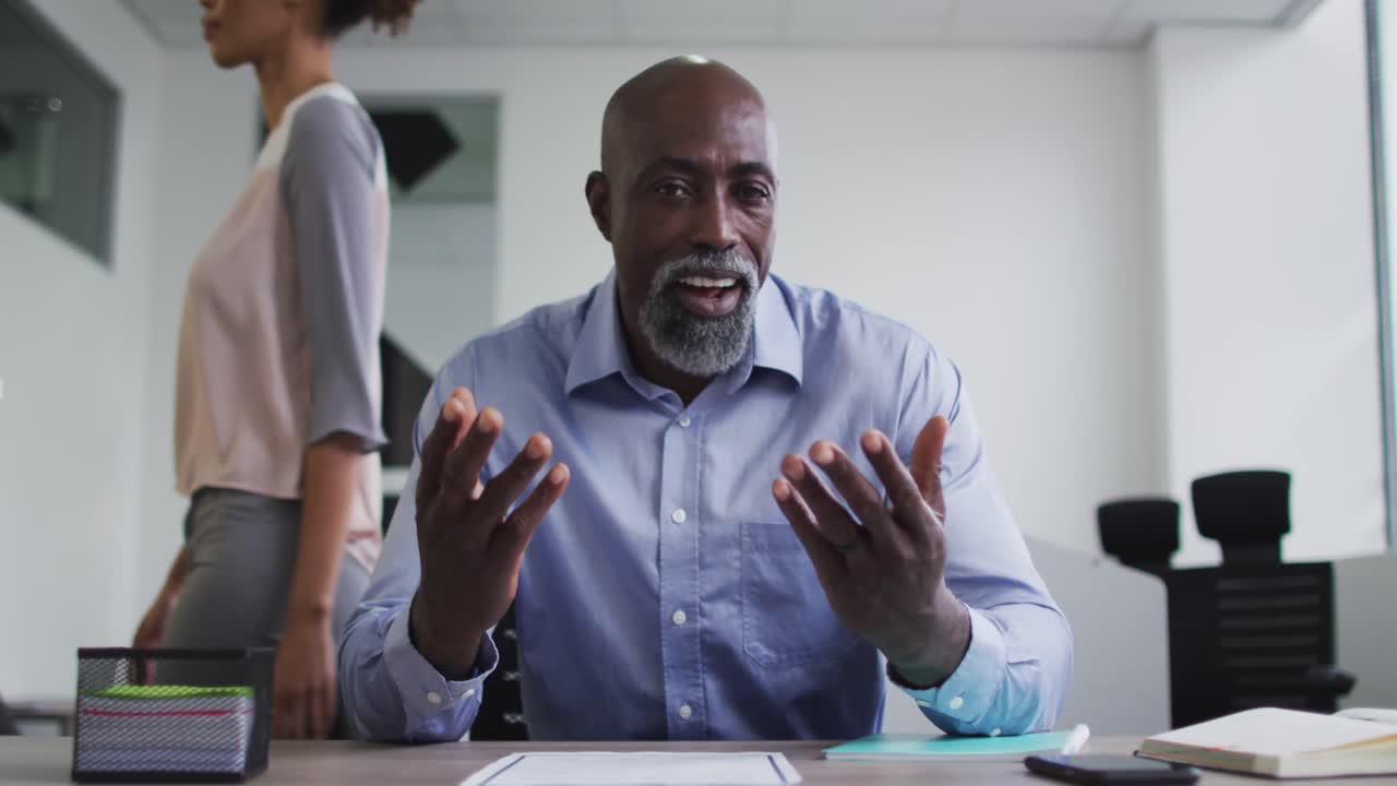 African american businessman sitting at desk and talking during video call in office