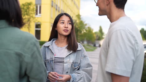 group of three happy young japanese friends standing outdoors and talking to each other