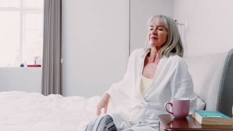 Senior-Woman-Waking-Up-And-Stretching-In-Bedroom