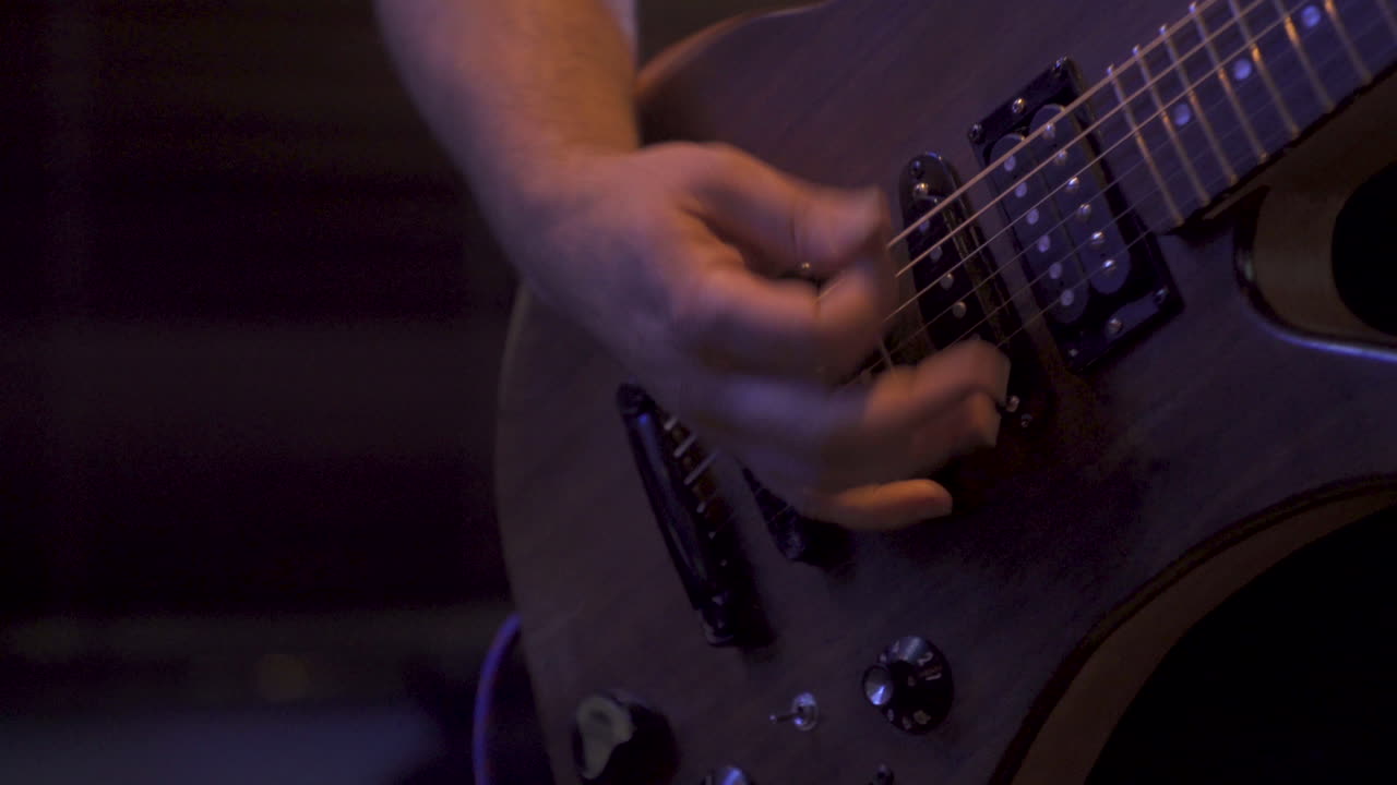 Primo piano in 4K di un artista che suona la chitarra con una band su un palco in un locale con luci soffuse.