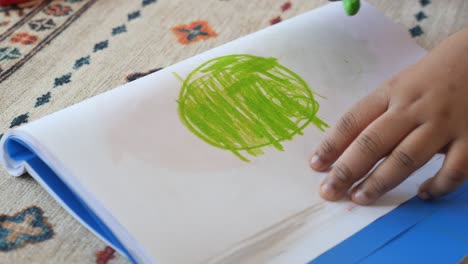 child drawing green circle with crayons