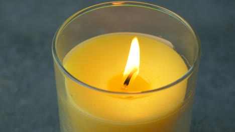 primer plano de una vela amarilla encendida en un soporte de vidrio