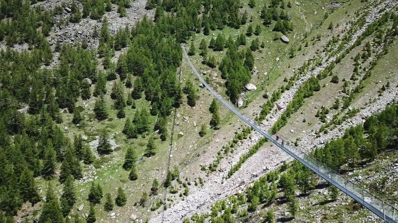 Breathtaking aerial footage of adventurous tourists crossing the modern bridge, nestled amidst the stunning alpine scenery, Charles Kuonen Hängebrücke Bridge, Randa, Wallis, Switzerland