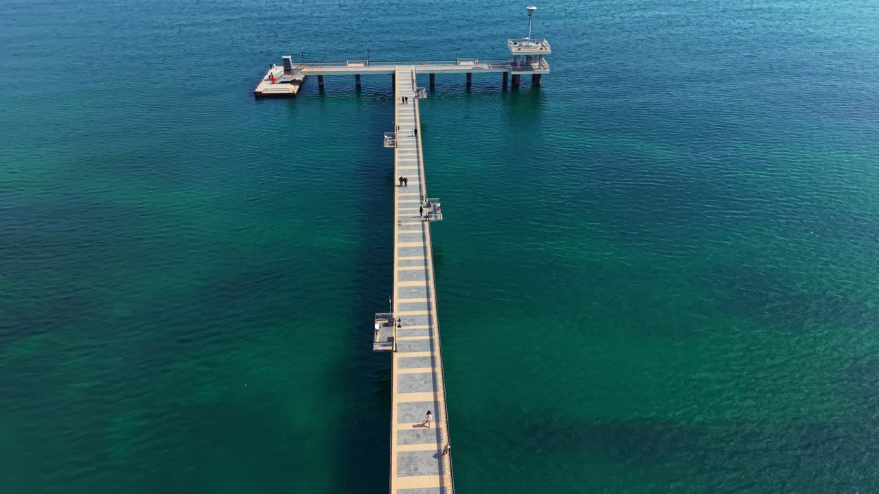 I visitatori camminano lungo un lungo molo di legno sopra acqua limpida e blu a mezzogiorno vicino a una zona costiera.