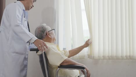 doctor and old asian man sits in a wheelchair and looks out the window. health care and insurance, retirement concept